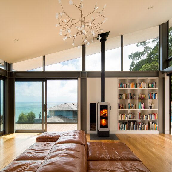 Holz-Kaminofen bionic fire EVO in der Farbe Schwarz mit weisser Vollglas-Feuerraumtüre im Wohnzimmer am Meer