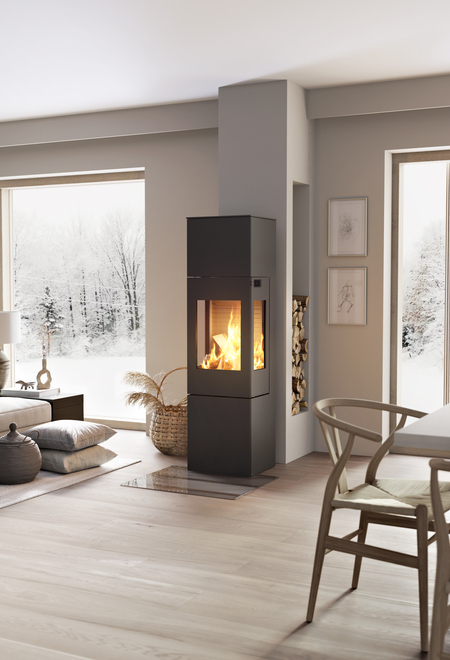 Poêle à bois NEXO 160 en noir avec porte en acier et vitres latérales au milieu de la pièce à vivre entre la salle à manger et le salon